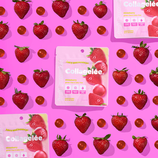 Image showing strawberry collagen infused gummy packets and fresh strawberries arranged on a pink background.