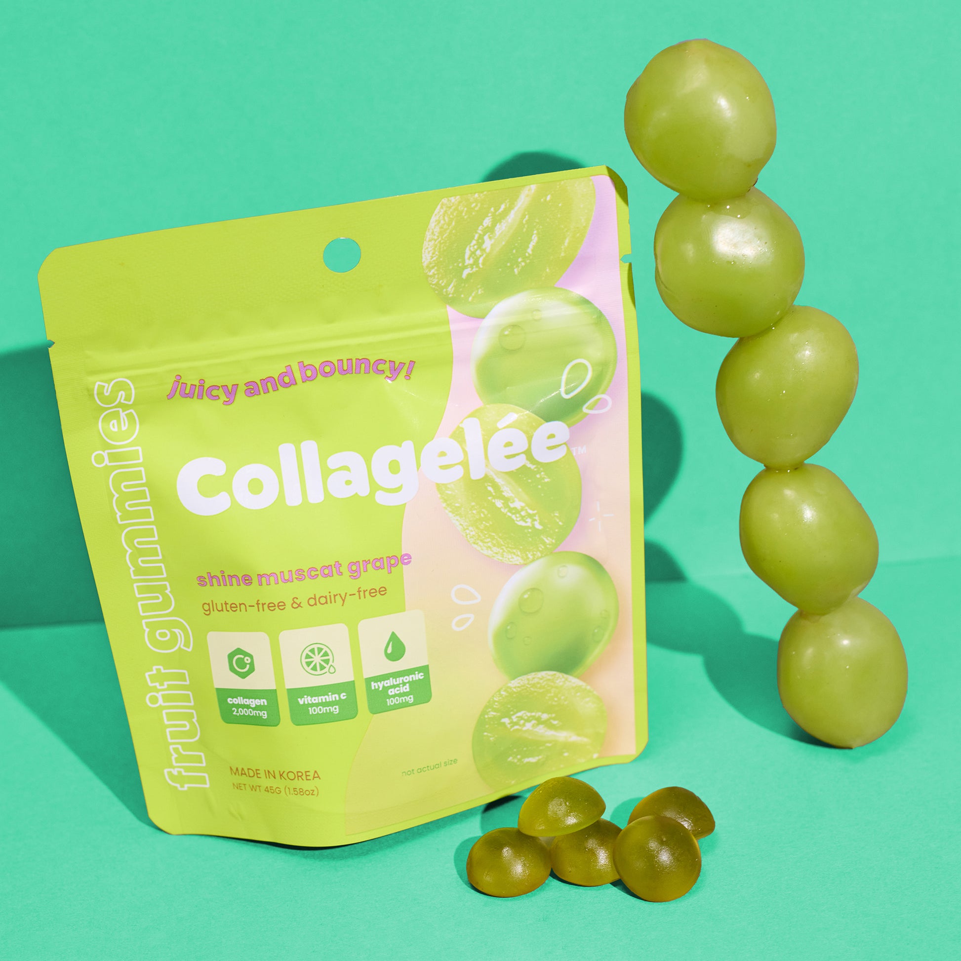 A neon green bag filled with Shine Muscat Grape Collagen-Infused gummies, next to stacked green grapes, highlighting the freshness of the fruit and the product.